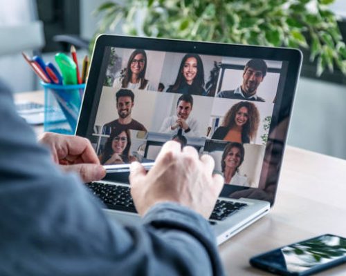 TRAINING Back view of male employee speaking on video call with diverse colleagues on online briefing with laptop at home.